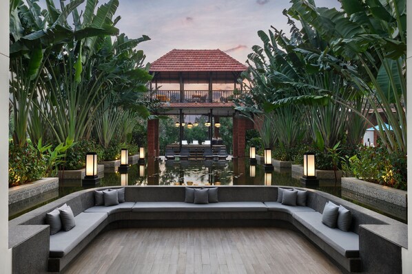 A serene outdoor seating area with a curved bench, surrounded by lush greenery and a reflective water feature. - The Westin Goa (Anjuna)