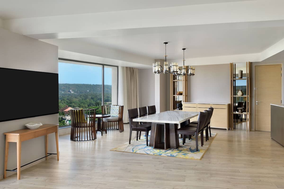 A modern dining area with a large table and chairs, a chandelier, and a view of the outdoors.