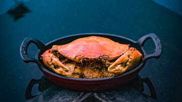 A red cast iron skillet with a cooked crab on a wooden table.
