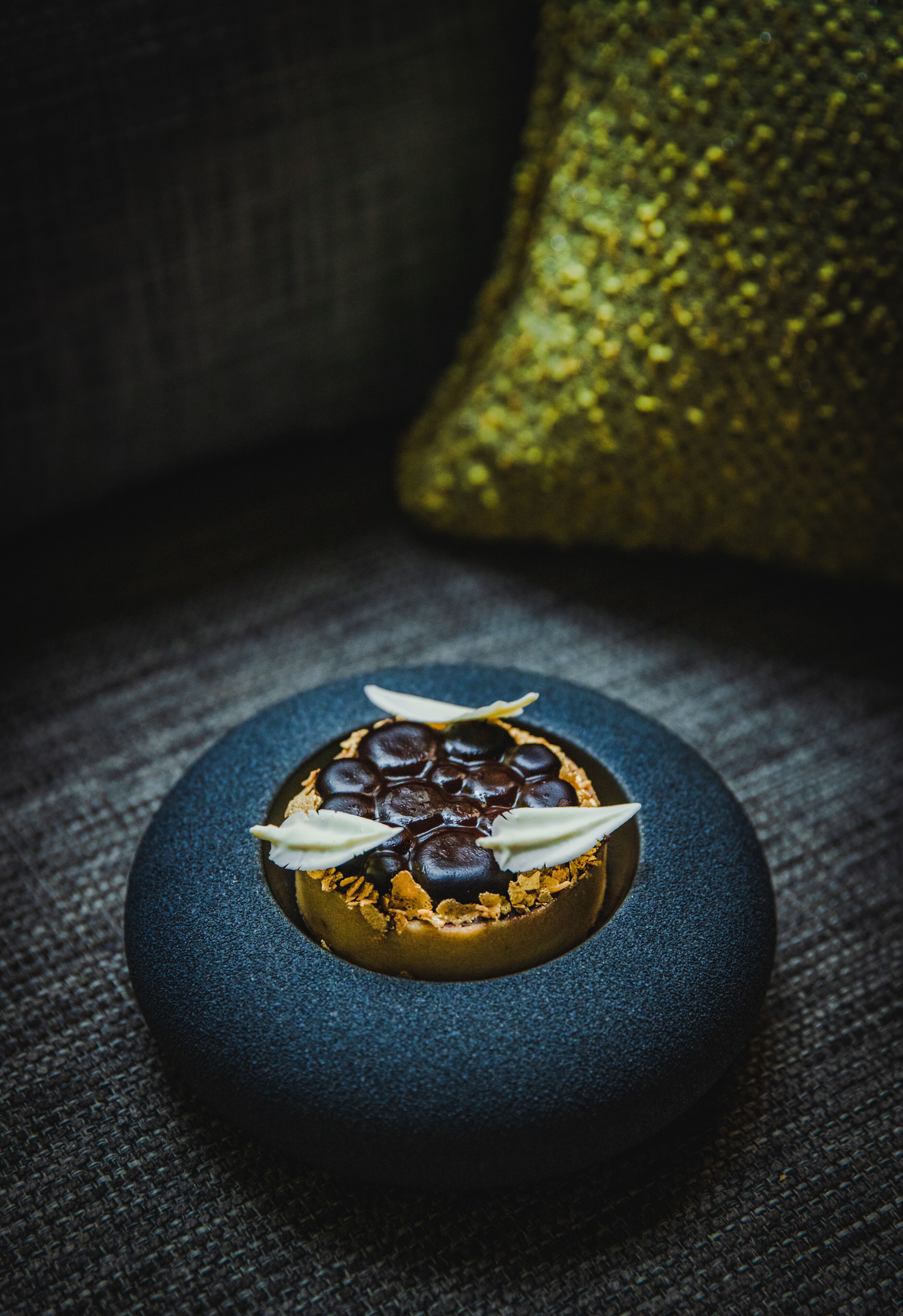 A dessert on a textured blue plate with a textured background and a glittery object in the background.