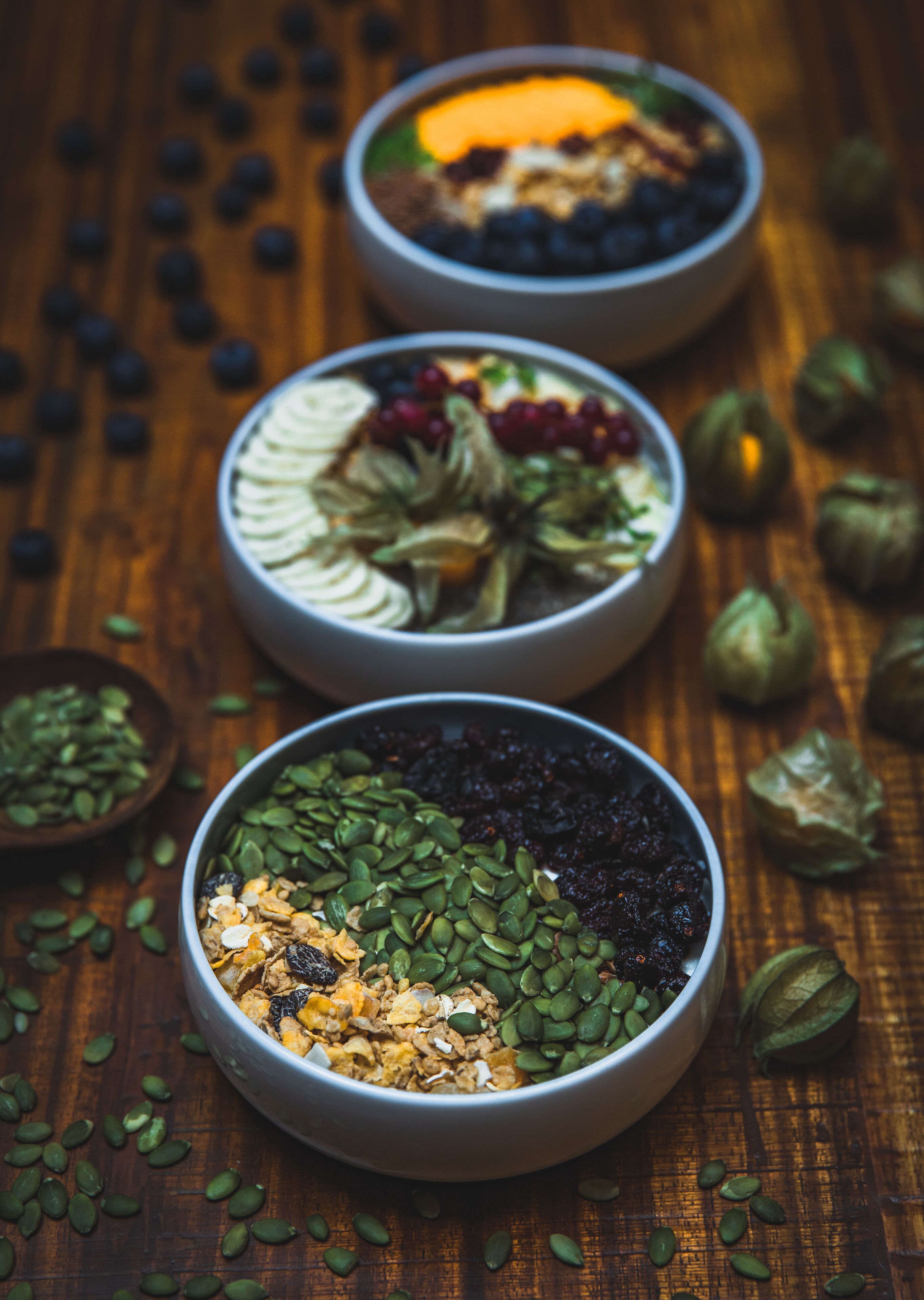 Three bowls of granola with various toppings on a wooden surface.