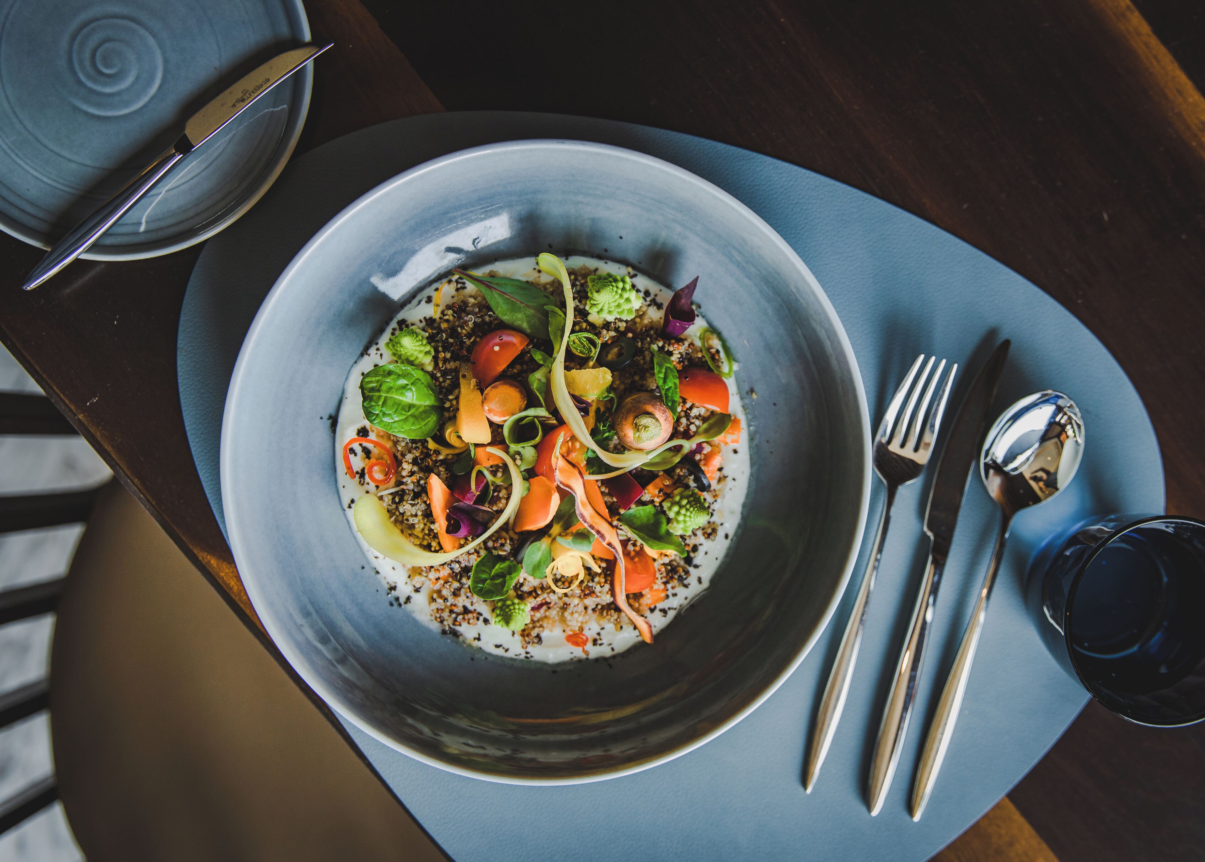 A bowl of salad on a plate with a fork and spoon beside it.