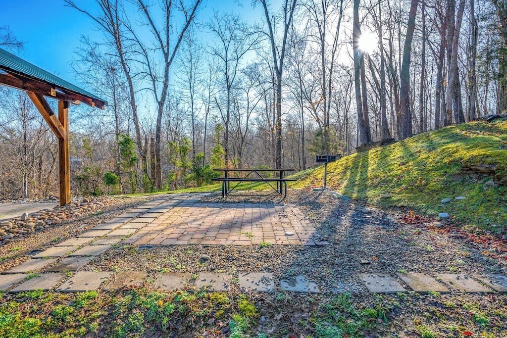 A picnic area with a bench and a shelter, surrounded by trees and a stone pathway.