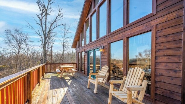 Terraza de madera con sillas Adirondack y una mesa, con vistas a un área boscosa.