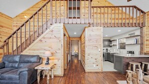 Amplia sala de estar con una escalera de madera, un sofá de cuero, una mesita con una lámpara y una cocina equipada con electrodomésticos modernos.