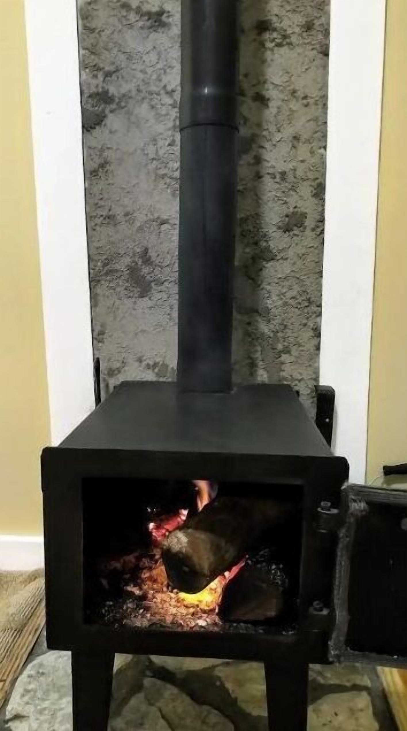 A wood-burning stove with a chimney, placed against a textured wall.