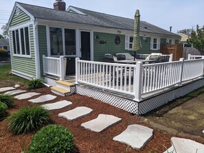 A green house with a white porch, stone steps, and outdoor furniture.