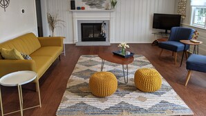 A living room with a yellow sofa, a blue armchair, a fireplace, and a TV. - Walk to the beach- Completely renovated 3 bedrooms house, central A/C (Dennis)