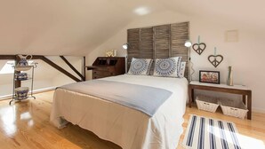 Un dormitorio con techo inclinado, una cama con almohadones estampados, una mesita de noche con lámpara y un adorno colgante en la pared.