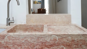 Un baño con lavamanos de mármol, un grifo moderno y un espejo que refleja una zona de comedor.