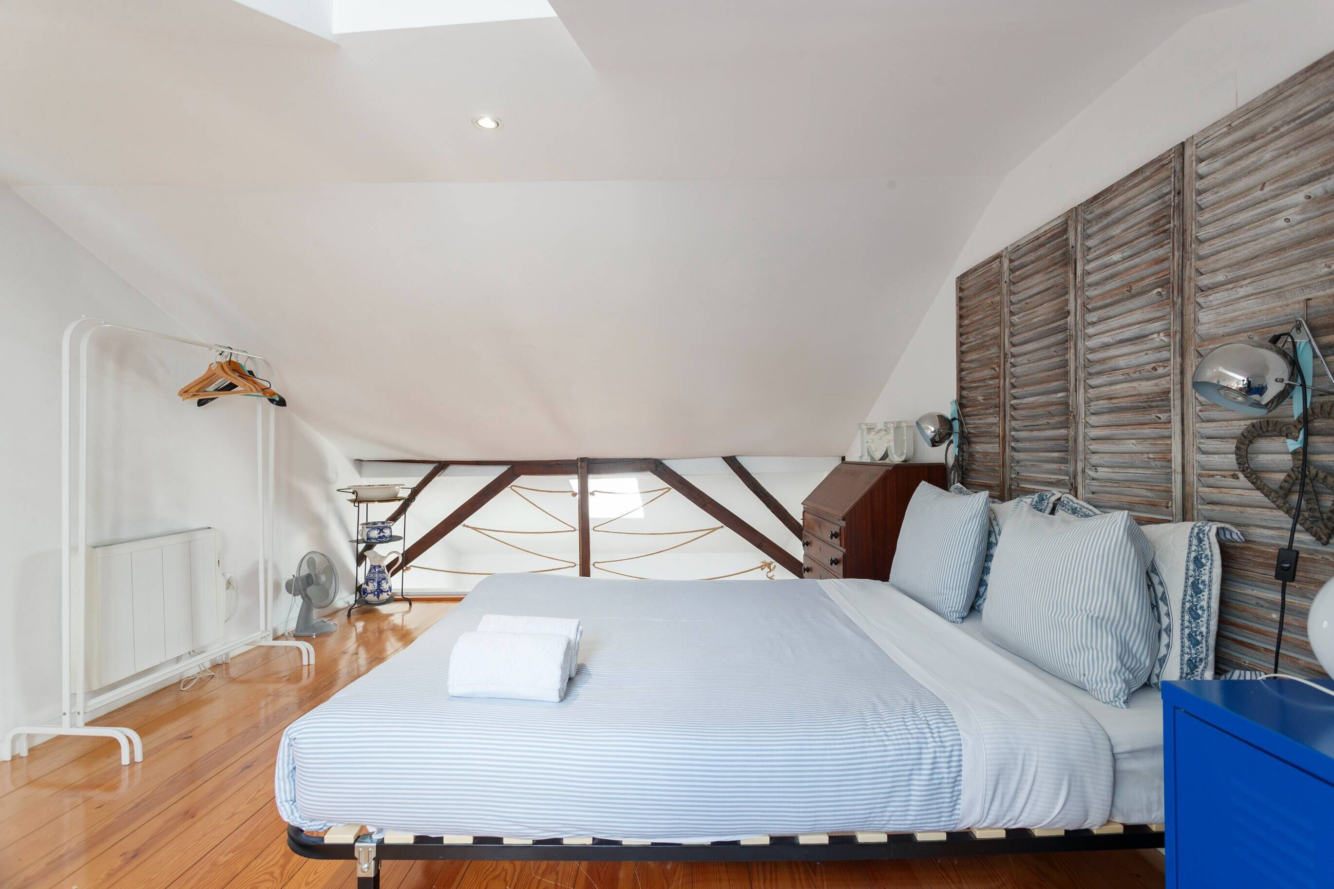Un dormitorio con cama, cabecero de madera, lámparas de noche y un aparador azul.