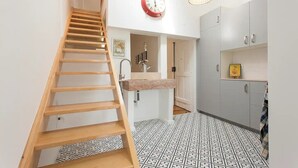 Una cocina moderna con una escalera de madera, un reloj rojo y una lámpara colgante.