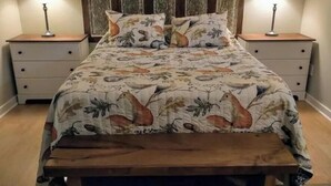 Ein Bett mit Blumenmuster auf der Tagesdecke, zwei Nachttische mit Lampen und eine Holzbank am Fußende des Bettes.