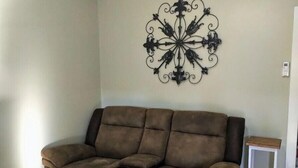 Ein Wohnzimmer mit einem braunen Sofa, einem Wandkunstwerk und einem kleinen weißen Beistelltisch.