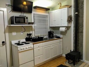 Compact kitchen with a stove, microwave, and sink, featuring white cabinets and a small table.