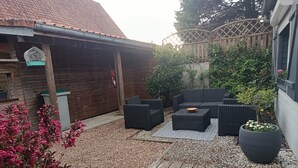En træterrasse med udendørs møbler, brandslukker og en have med beplantning samt et plantet træ.