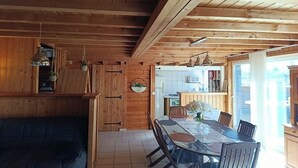 Et interiør med trævægge, et spisebord, stole, en sofa og et køkkenområde.