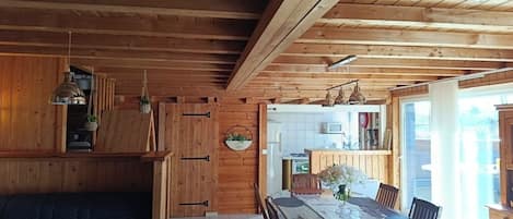 A wooden interior with a dining table, chairs, a sofa, and a kitchen area.