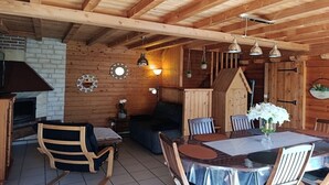 Et træpanelt interiør med et spisebord, stole, en pejs og hængende lysarmaturer.