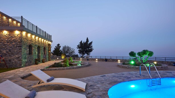 A pool area with lounge chairs and a stone building with lights. - Irma Villa, a Secluded Sanctuary (Krousonas)