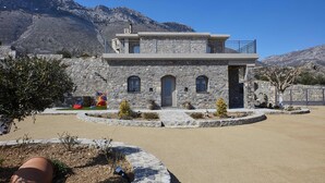 A stone building with a balcony, a driveway, and a mountain backdrop. - Irma Villa, a Secluded Sanctuary (Krousonas)