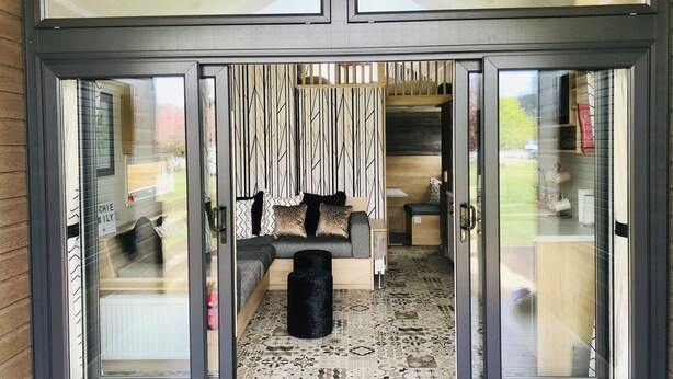 A modern interior with a sofa, patterned curtains, and a black cylindrical object. - 2 Bed Lodge - Sleeps 4 - Pets - Hot Tub - Parking (Inverness)