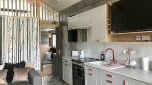 A compact kitchen with white cabinets, a built-in oven, and a large TV. - 2 Bed Lodge - Sleeps 4 - Pets - Hot Tub - Parking (Inverness)