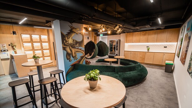 Ein modernes Interieur mit einem runden Holztisch, Barhocker, einer grün gepolsterten Sitzecke und einer wandmontierten Vitrine.