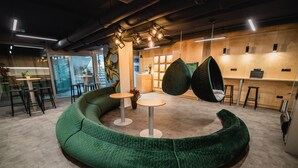 Ein modernes Interieur mit einer grünen, gebogenen Sitzgruppe, Hängesesseln und einer Bar.