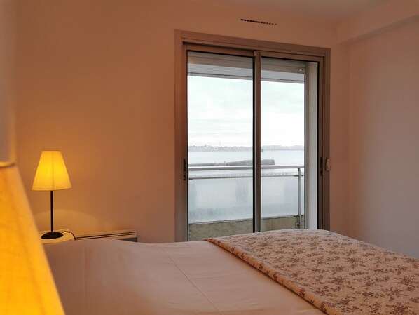 Une chambre d’hôtel avec un lit, une lampe et une vue sur une étendue d’eau, visible par une grande fenêtre.