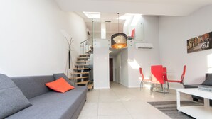 Una sala de estar moderna con un sofá gris, sillas rojas y una mesa de centro blanca. Una escalera conduce a un nivel superior.