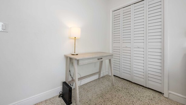 A room with a white wall, a wooden console table with a lamp, a closed white closet, and a speckled floor. - URBAN4-1 | relax after exploring Brickell City (Miami)