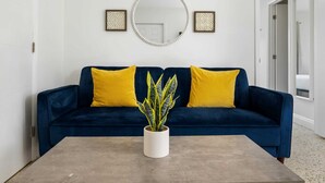 A room with a dark blue sofa, two yellow cushions, a round mirror, and a potted plant on a grey table. - URBAN4-1 | relax after exploring Brickell City (Miami)