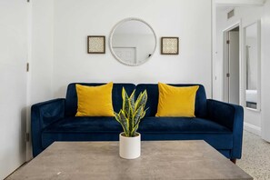 A room with a dark blue sofa, two yellow cushions, a round mirror, and a potted plant on a grey table. - URBAN4-1 | relax after exploring Brickell City (Miami)