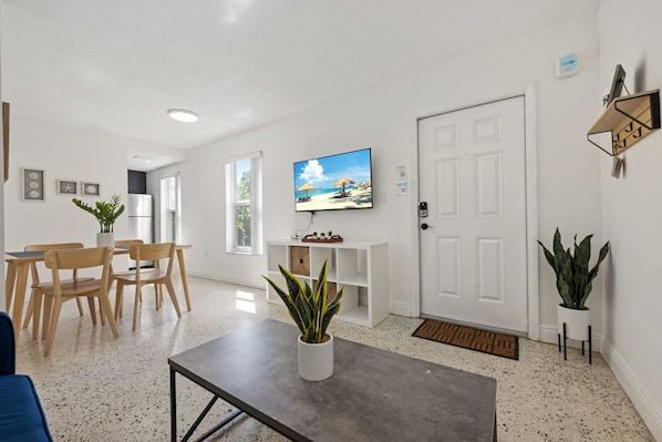 A modern living room with a dining area, a television mounted on the wall, and a door with a key lock. - URBAN4-1 | relax after exploring Brickell City (Miami)