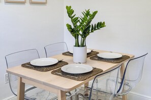 Una mesa de comedor con cuatro platos, un jarrón blanco con hojas verdes y sillas transparentes.