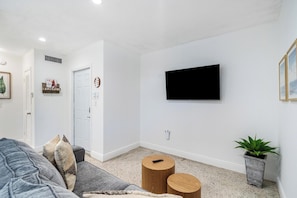 Ein modernes Wohnzimmer mit einem flachbildfernseher an der Wand, einem grauen Sofa, zwei Holztischen und einer Zimmerpflanze.