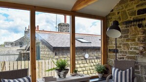 A cozy room with a stone wall, large windows, wicker furniture, and a wooden desk with plants. - 2 bedroom accommodation in Addingham, near Ilkley (Addingham, near Ilkley)