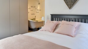 A bedroom with a bed, pillows, a headboard, a wall-mounted heart-shaped decoration, and a bathroom visible through an open door. - 2 bedroom accommodation in Addingham, near Ilkley (Addingham, near Ilkley)