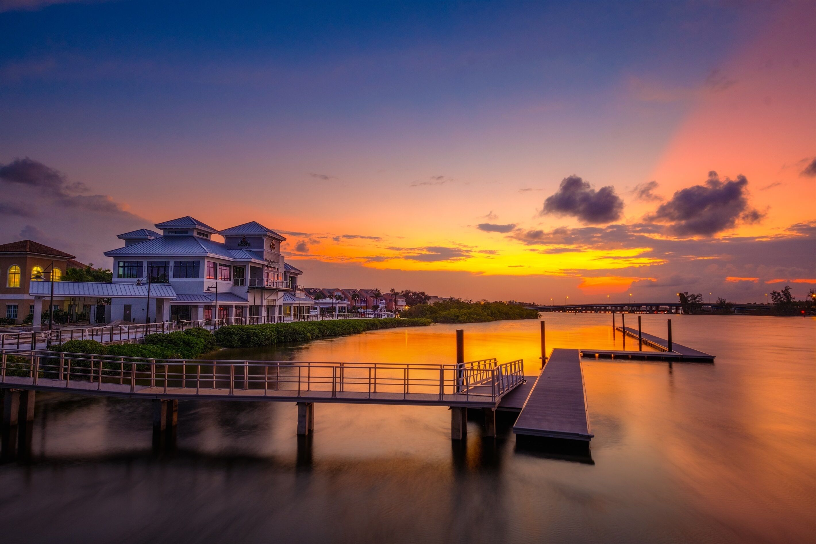 A waterfront property with a dock, a large building with multiple levels, and a sunset view.