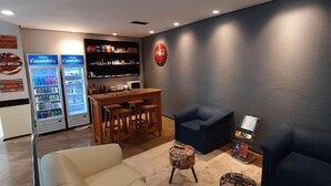 A modern lounge area with a sofa, armchairs, a small table, and a refrigerator. - Partner Hotéis by Holz (Joinville)