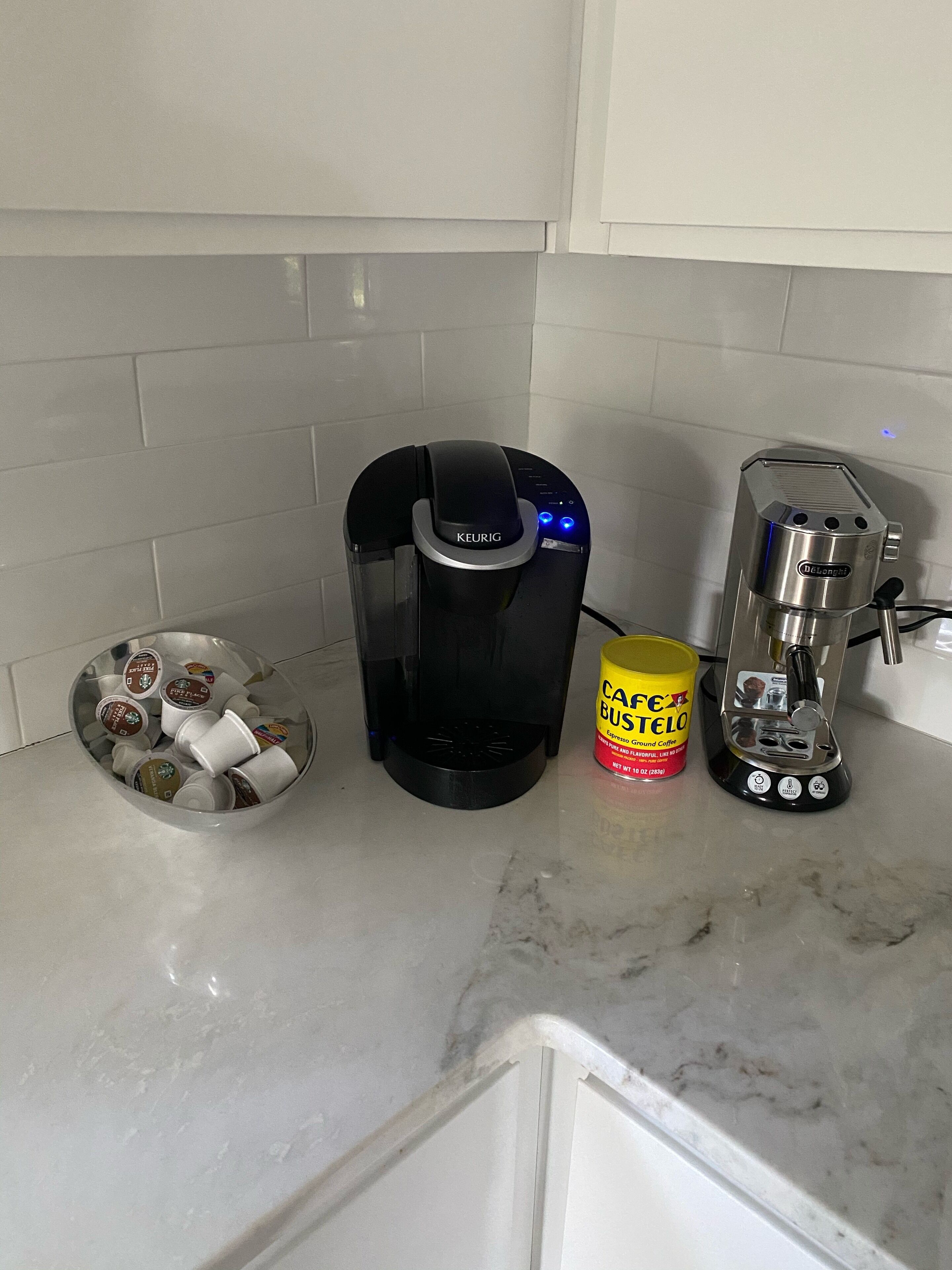 A coffee maker, a container of coffee pods, and a coffee grinder on a kitchen counter.