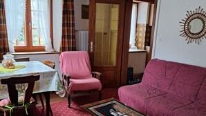 Una sala de estar acogedora con una alfombra roja estampada, un sillón rosa, una mesa de centro de madera con un cuadro enmarcado y una puerta de madera con un panel de vidrio.