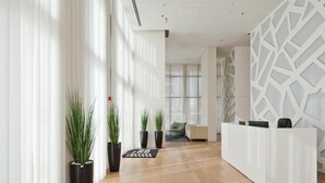 Een moderne receptie met een wit receptiebalie, potplanten en een geometrisch wandontwerp.