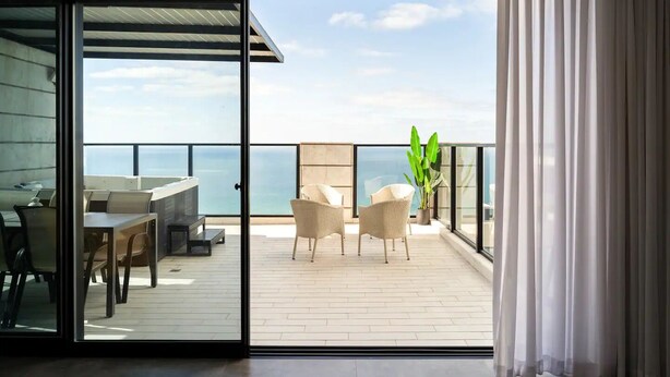 Een balkon met uitzicht op zee, een tafel met stoelen en een potplant.