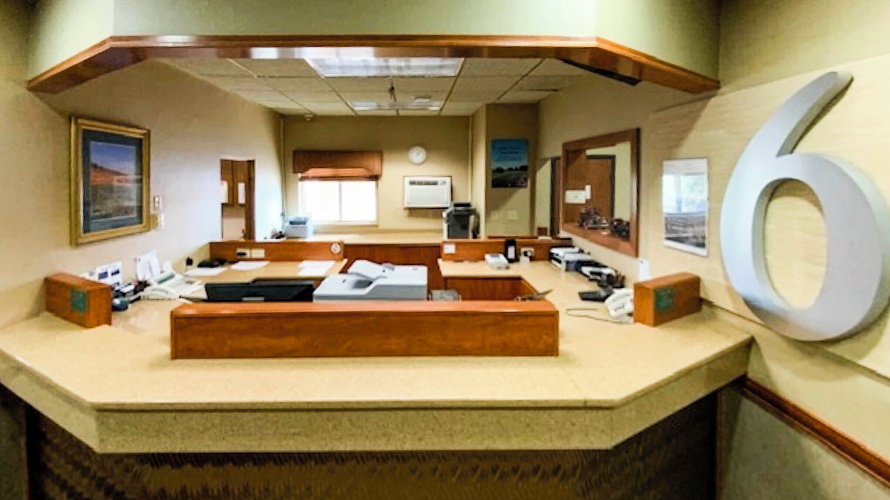 A reception desk with a large number '6' on the wall, a clock, and a window with a view.