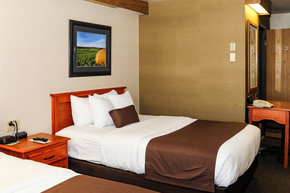 A hotel room with two beds, a desk, and a framed picture on the wall.