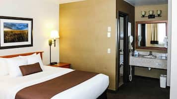 A hotel room with a bed, a bedside lamp, a framed picture on the wall, a bathroom with a sink and mirror, and a telephone.