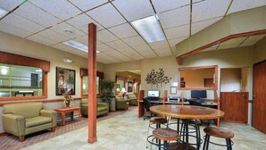 A spacious lobby with a central round table and bar stools, a comfortable sofa, a large mirror, and a decorative wall piece. - Studio 6 Minot, ND (Minot)