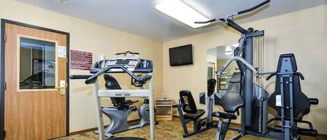 A hotel room with a treadmill, exercise bike, and weight bench.
